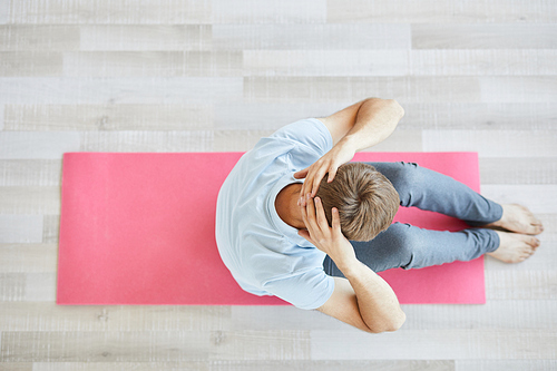Overview of active man in sportswear sitting on pink mat and exercising alone