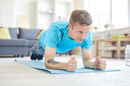 Young active man in blue t-shirt doing planks on the floor of living-room at home