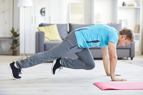 Young active man bending over floor while working out in living-room at home