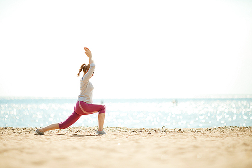 Side view of active female doing exercises for leg stretch and arms by waterside