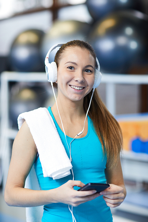 Happy sportswoman with headphones listening to music at break between workouts in fitness center