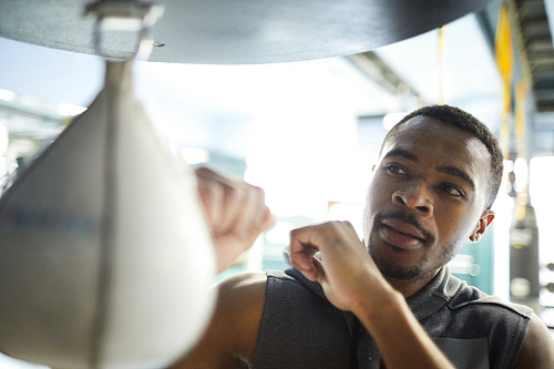 Young African-american athlete exercising with punching bag in modern leisure center or gym