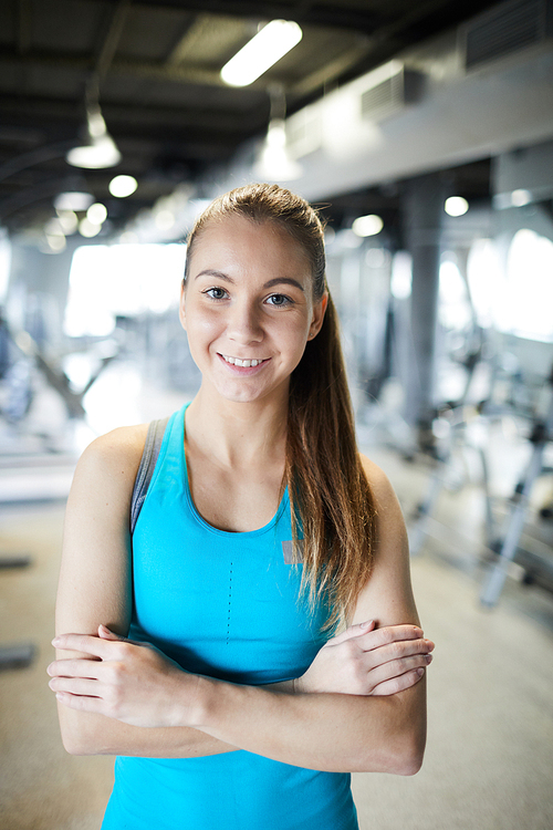 Young cross-armed active woman standing in front of camera in fitness center