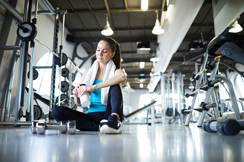 Young fit woman sitting on the floor after workout and going to have some water from plastic bottle