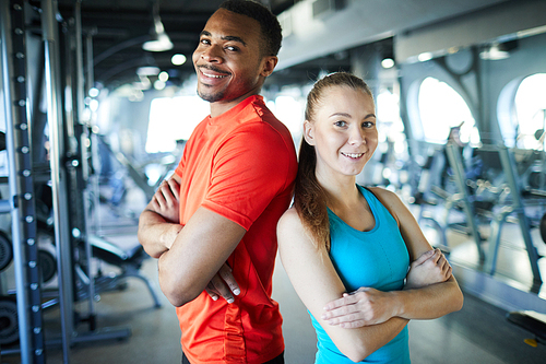 Young sports professionals or athletes in activewear standing back to back in modern fitness center