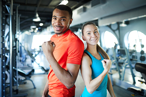 Young successful sports coaches in activewear showing gesture of strength while looking at you