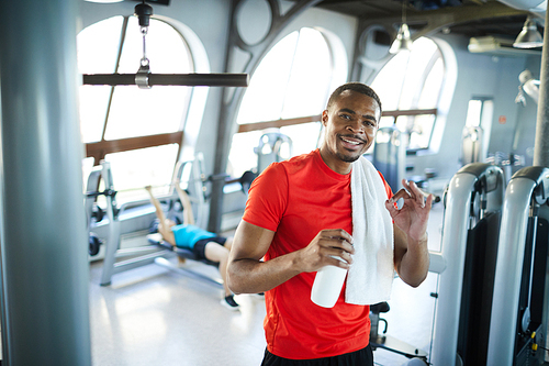 Happy young afroamerican sportsman with towel and bottle of water enjoying break after hard training in gym