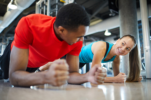 Happy active girl making plank and looking at her mate during exercise in fitness center