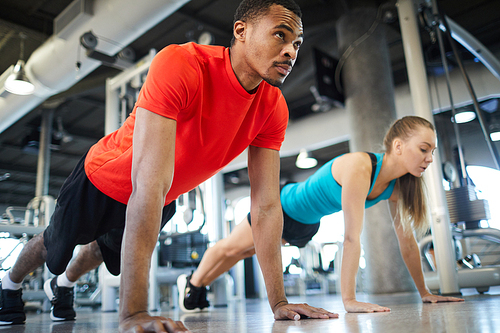 Young man and woman in activewear doing press-ups on the floor of fitness center