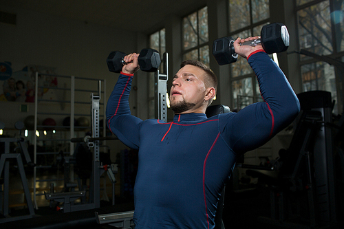 Strong muscular young man in sportswear exercising with dumbbells