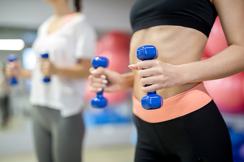 Midsection of fit girl exercising with blue dumbbells in modern sports club