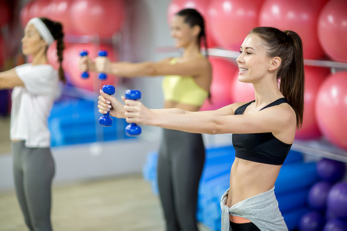 Happy young sportswoman with dumbbells and her friends exercising in contemporary fitness center