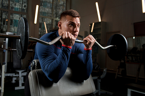 Muscular sportsman lifting heavy weight during training in gym