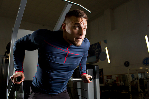 Strong sportsman holding by handles of sports equipment while exercising in gym