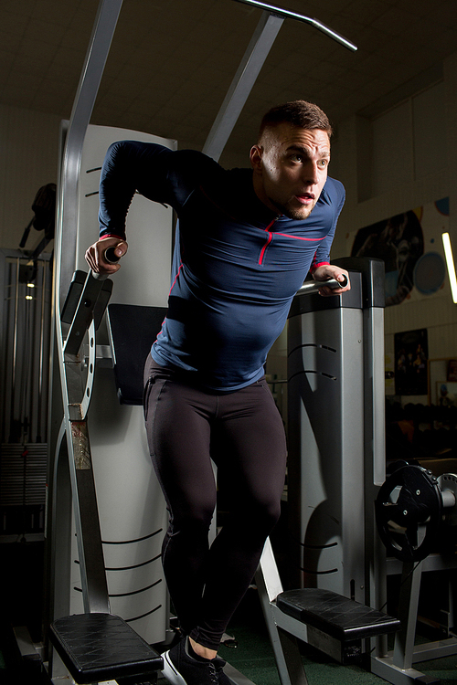 Young man pumping his arms on sports equipment during workout