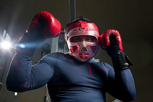 Young athlete in protective helmet and boxing gloves working out in gym