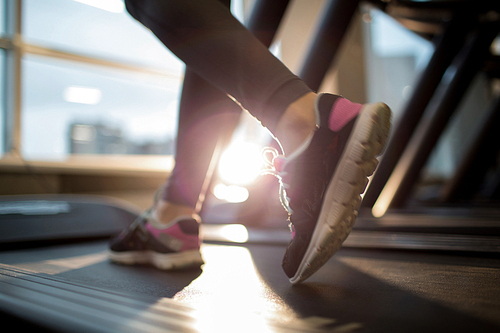 Sporty female feet in sports-shoes running down treadmill track in gym