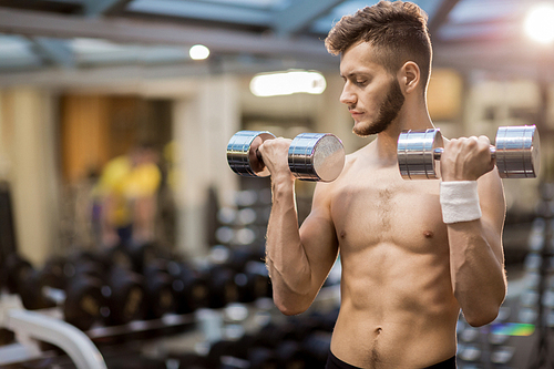 Young muscular man exercising with dumbbells while working out in fitness club