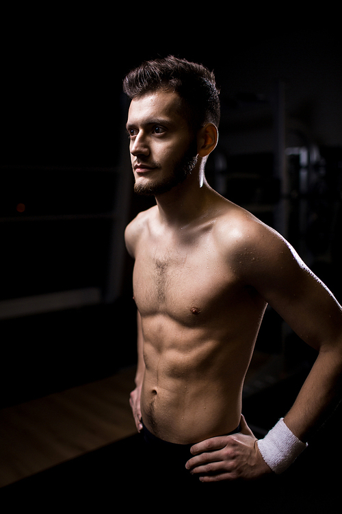 Shirtless athlete keeping his hands on waist and demonstrating his muscular torso during workout