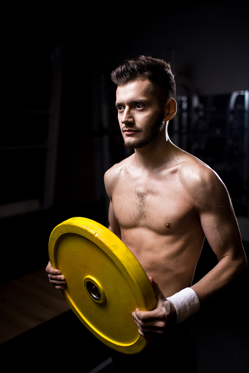 Young shirtless muscular man with heavy barbell disc