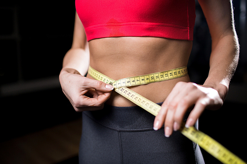 Young slim female measuring her waist after extensive physical training