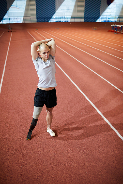 Bald sportsman with handicapped leg exercising on racetrack on contemporary stadium before workout