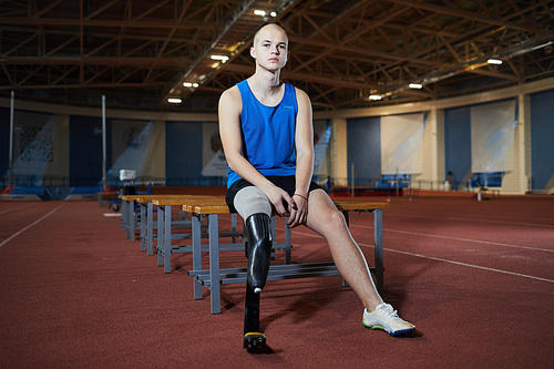 Young paralympic runner with artificial right leg sitting on bench after marathon on stadium