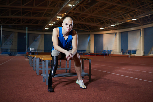 Young man in activewear sitting on bench while having break between trainings for paralympic games