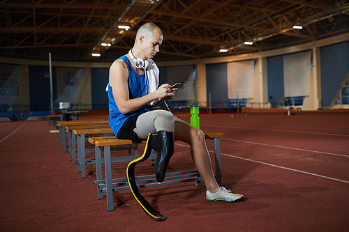 Active guy with handicapped right leg scrolling in his smartphone while having break after workout