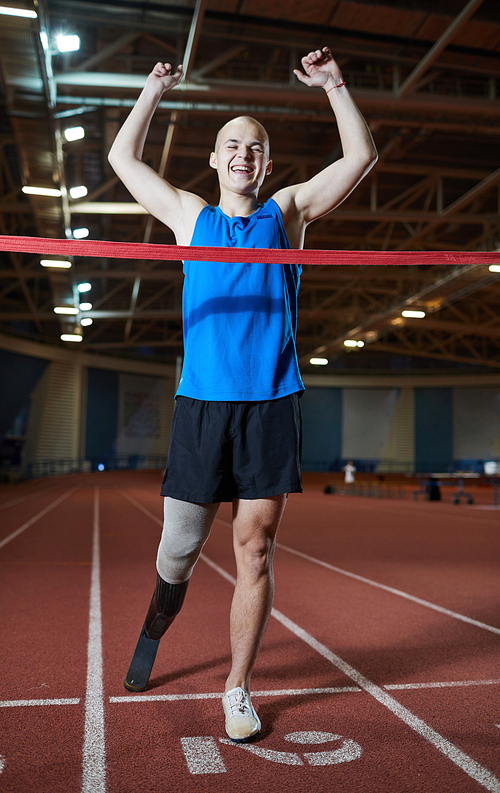 Happy and successful young paralympic sportsman with raised arms reached finish line during competition