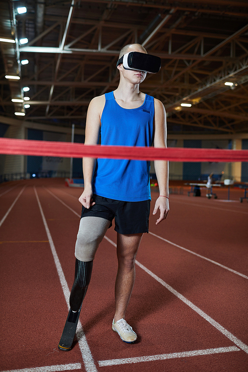 Young active man in sportswear watching video in virtual reality headset while standing by finish line on race track