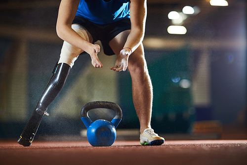 Young paralympic athlete leaning over heavy kettlebell before taking and lifting it during workout