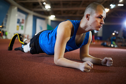 Young paralympic sportsman standing in plank on the floor of stadium while training before competition