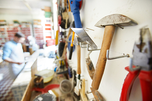 Close up shot of working tools on wall stand with blurred shapes on people in background, copy space