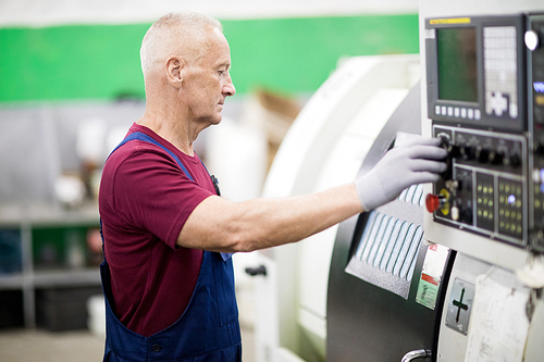 Concentrated skilled manufacturing specialist working with computer machine in factory