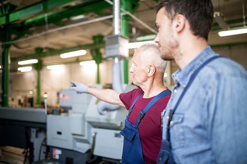 Mature foreman showing workplace to his colleague in factory