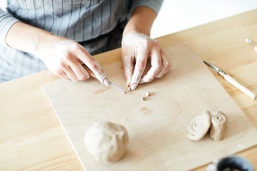 Master of pottery cutting thin piece of clay into small pieces on wooden board