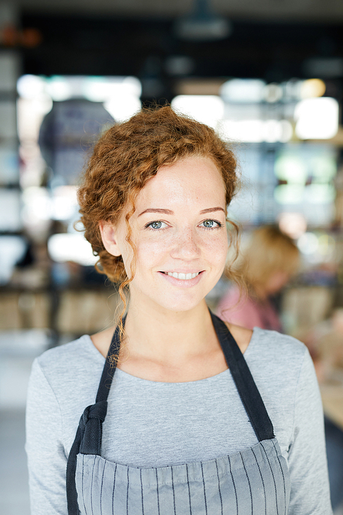 Happy young woman with toothy smile wearing apron during work in studio of pottery