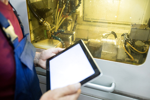 Touchpad in hands of modern engineer standing by transparent door of industrial machine with bunch of wires behind