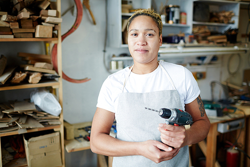 Female woodworker holding drill and  while standing in workshop.