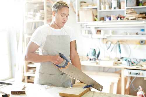 Female carpenter with handsaw working with wooden board in workshop
