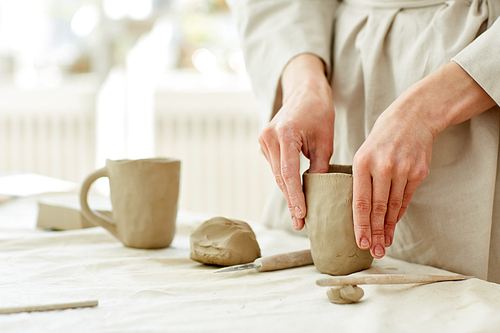 Female hands forming mug from grey clay while working in studio of handmade production