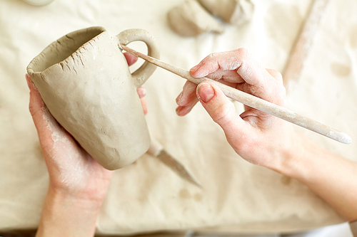 Hands of young master with handtool working with details of clay mug