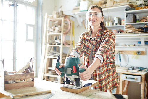 Happy young female carpenter with electric grinder  while working
