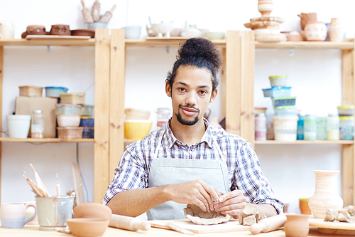 Portrait of young confident mixed race man modeling clay pot in workshop and 