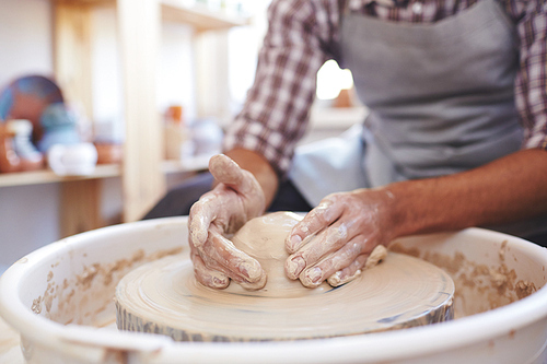 Unrecognizable male ceramist making clay jar on spinning pottery wheel in workshop, close-up view