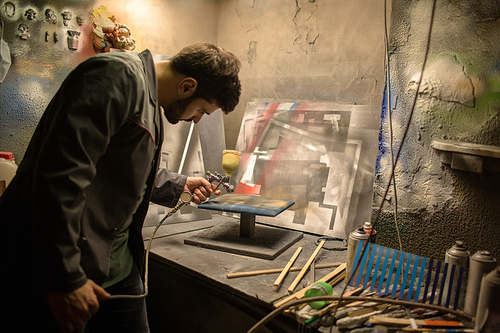 Young professional painter using special equipment for spray painting during work