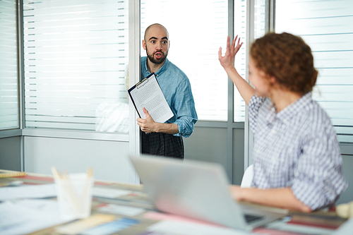 Stunned bald bearded assistant with papers barging into office of manager and showing contract condition, redhead lady asking him to get out of office