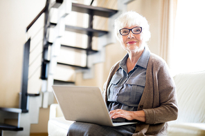 Aged grey-haired woman  while sitting on sofa and networking