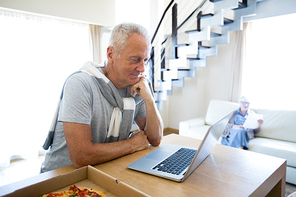 Contemporary senior businessman looking at laptop display and reading online data with colleague on background